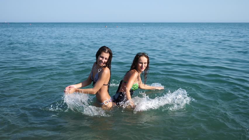 Two sexy girlfriends, brunette and red-haired are enjoying themselves in the sea. Sprinkle each other with water and have fun. Slow motion. 4K.