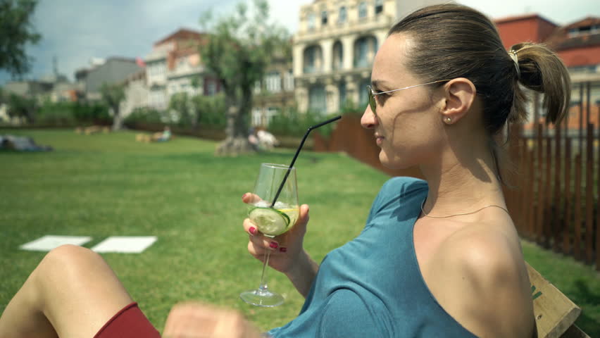 Young, happy woman dancing and drinking cocktail in garden in cafe
