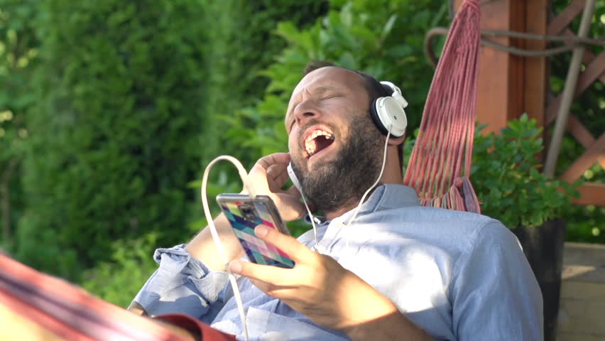 Man listening to music and singing lying on hammock in garden, super slow motion 240fps
