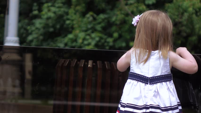 In the city park girl child through a glass railing looking at the fountain