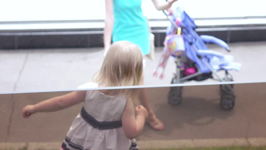 In the city park girl child through a glass railing looking at the fountain