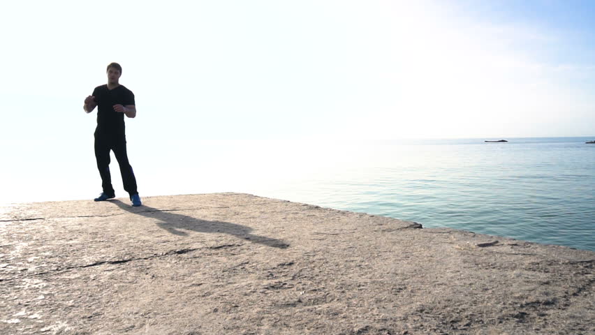 Young man does round house high kicks barefooted against sunrise in slow motion