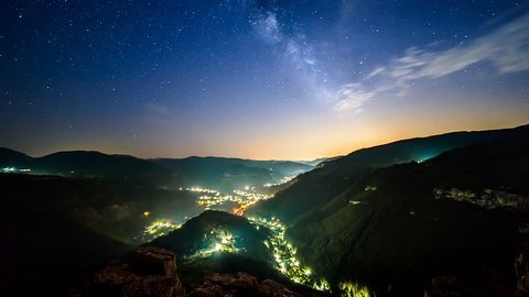 Timelapse of the milky way over a small city surrounded by mountains.