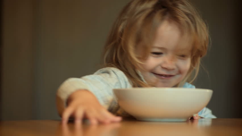 Child does not want to eat, cute child with long hair in pajamas in kitchen pushes out plate of food, breakfast or lunch. Boy is playing at the table in the morning. Nutrition and day regimen for baby Royalty-Free Stock Footage #29288341