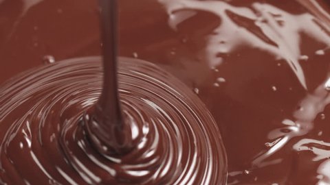 Slow motion pouring premium dark melted chocolate from big spoon
