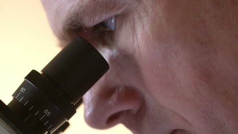 Close up of a mature doctor or laboratory researcher looking through the eyepiece of a microscope.