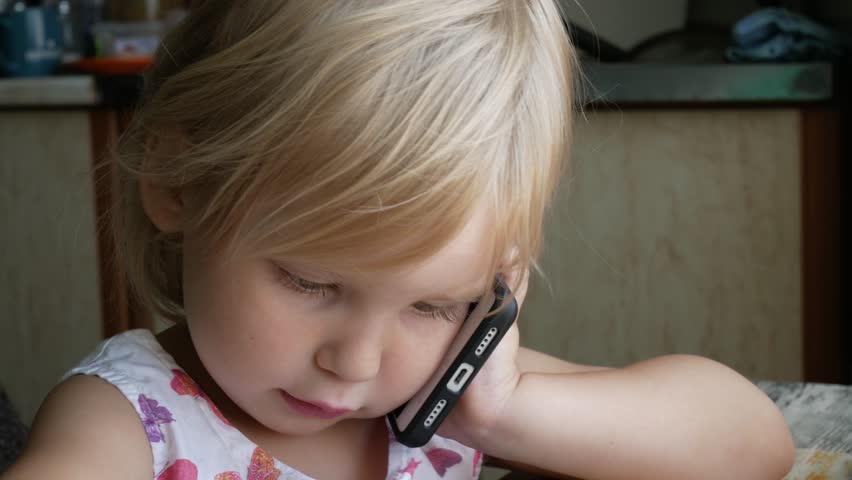 Little girl talking on mobile phone. Portrait of a three-year-old child who confidently holds the phone in his hand and talks.