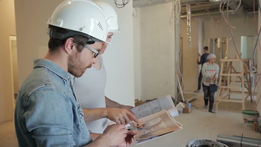 Among the repairs, two men in helmets discuss a project on securities. The construction team works for the reconstruction of the premises. People around color, clean and clean. A tall customer with a