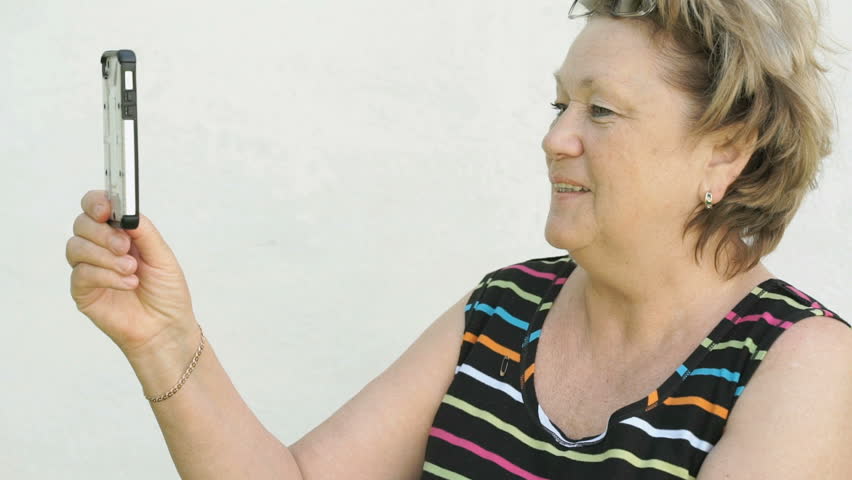 Adult woman blonde dressed in striped tank top talking with a husband using smart phone outdoors