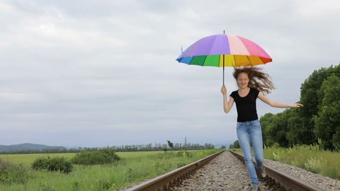 Teen girl with umbrella jumping on the railway at the day time. Concept of happiness.