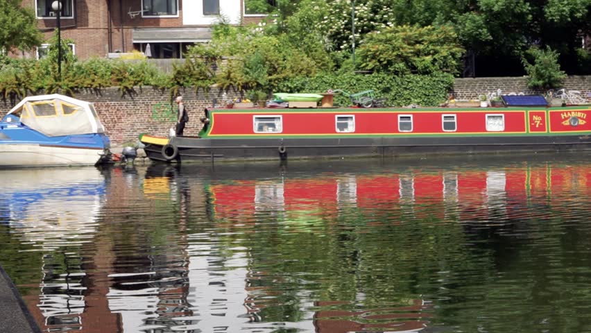 Brightly painted canal boats houseboats and a motor pleasure boat moored in London canal under a blue sky on a sunny day as a person rides a bicycle on the towpath