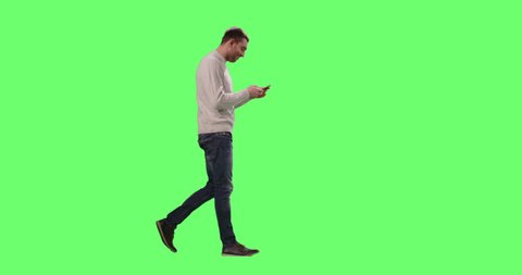 Casual Caucasian Man is Walking and Using Smart Phone on a Mock-up Green Screen in the Background. Shot on RED Cinema Camera in 4K (UHD).
