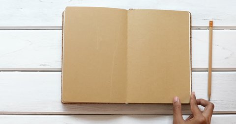A male hand open diary brown paper 6 page then close  on the white wooden desk, top view and overhead shot use for blank template book mock up to add any text content, 4K Dci resolution