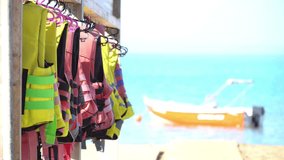 Watersport adventure background video - colorful life vests on a beach rack with a boat and waves in the background