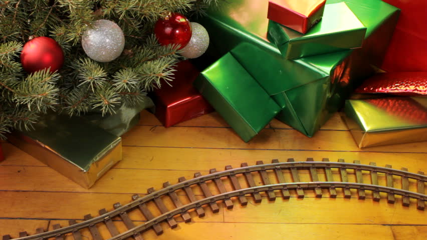 Toy electric train filled with decorations passes along wood floor on Christmas