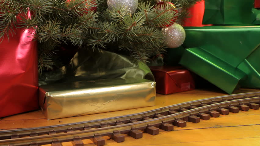 Toy electric train filled with decorations passes in front of christmas tree