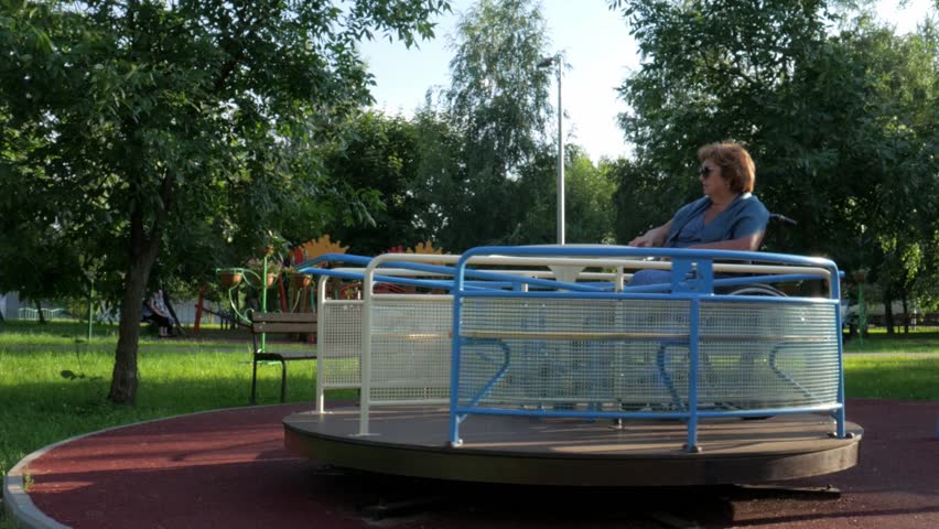 Woman in roundabouts. A mature female in the wheelchair is riding roundabouts in the park.