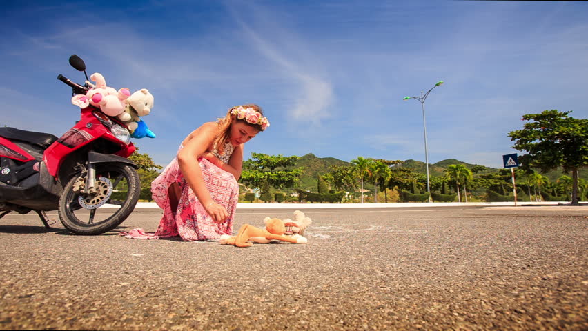 young beautiful lady in long pink dress and garland squats by red motorcycle and draws in street against plants and sky