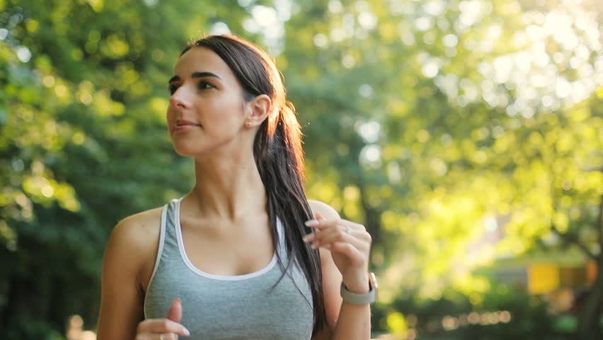 Handsome woman runing through the park in the morning during sunrise. Portrait shot.