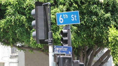 Low Angle of street sign and traffic lights at corner of Sweetzer Avenue and 6th Street with trees in the background