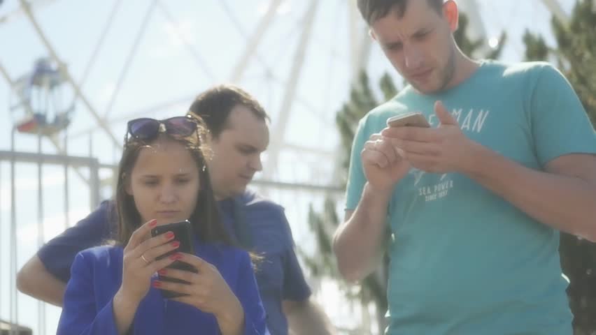 A group of friends the guys and a girl stand with the phones in their hands and look at them, they study the map. HD, 1920x1080. Slow motion