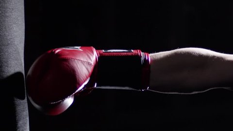 Fighter Practicing Some Kicks With Punching Bag - A Man With A Tattoo Boxing On dark Background. Kick, punching bag on dark background. Black punching bag weighs at the gym