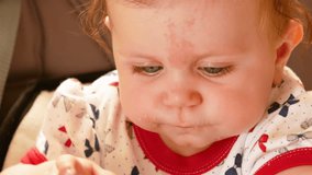 Mom feeds from spoon her little seven-month-old daughter with blond hair. In the chair for feeding. A child with a birthmark on his forehead. 4k video
