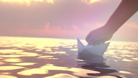 Kid putting a paper boat into water over beautiful sunset. Little boy's hand puts paper ship on sea surface. Origami ship Sailing. Dreams, future, childhood, freedom or hope concept. Slow motion 4K