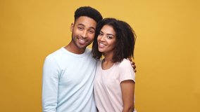 Happy cheerful african man showing thumbs up gesture and hugging his girlfriend isolated over yellow background