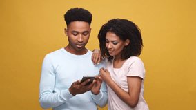 Happy young couple watching a funny video on mobile phone together isolated over yellow background