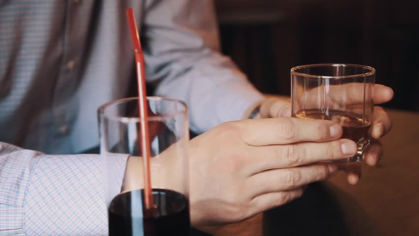Male hands of unrecognisable man in plaid shirt holding glass of whiskey upon table with cola at bar | Shutterstock HD Video #29363743