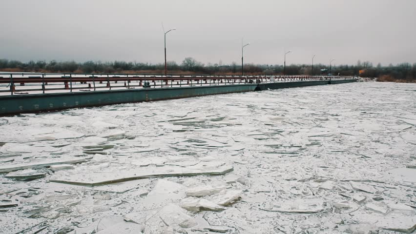 Metal ferry bridge over shuttered ice frozen river surface covered in snow, cold winter cloudy day
