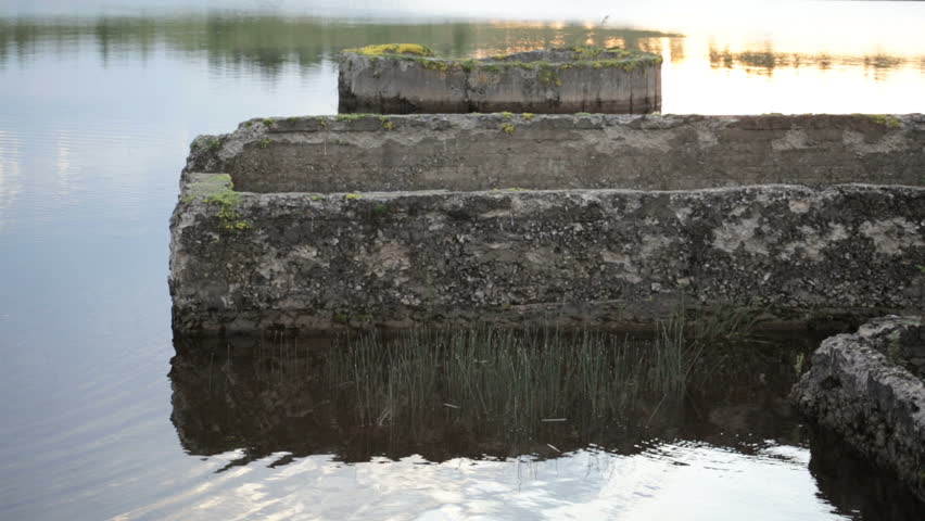 A man is riding on a SUP board in the evening among flooded ruins