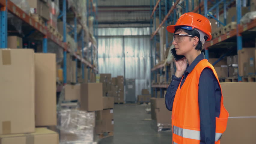 woman worker in storehouse using wireless barcode scanner scanning labels on boxes before delivery in logistic center. professional employee wearing uniform high visibility orange hard hat and vest Royalty-Free Stock Footage #29372755
