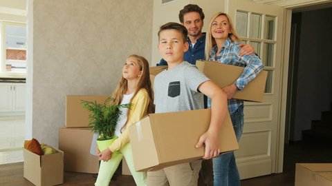 Portrait of young exaciting family carrying cardboard box into the new modern home to the living room.