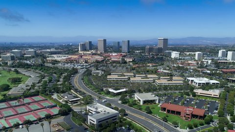 Aerial timelapse in motion (hyperlapse) from a drone of Fashion Island shopping center skyline in Newport Beach, California with office buildings, traffic, mountains and clouds overhead.