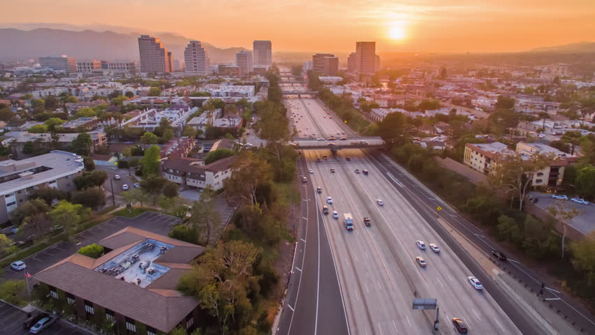 Aerial timelapse in motion (hyperlapse) overhead shot at sunset in LA at twilight with the sky changing from day into night with golden skies. Sun sets behind city skyline and high rise buildings.