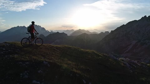Aerial - Flyover mountain biker standing on top of the mountain at sunset