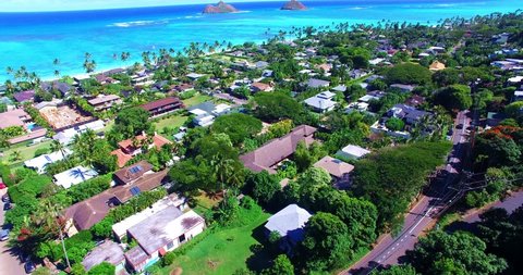 Flyover of Coastal Village Neighborhood and Road Near Sandy Beach with Two Small Islands in the Background - Aerial Footage of Oahu, Hawaii