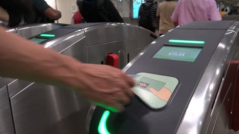 SINGAPORE - MAY 2017: Commuting subway passengers swipe cards to exit MRT (Mass Rapid Transit) station via turnstiles in Singapore