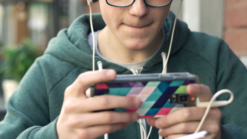 Young teenager watching movie on smartphone and eating fries sitting in cafe
