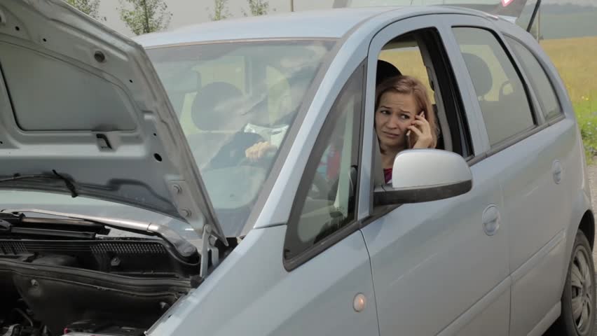 blonde girl calling cellphone in a panic sitting in her broken car with open hood on a country road