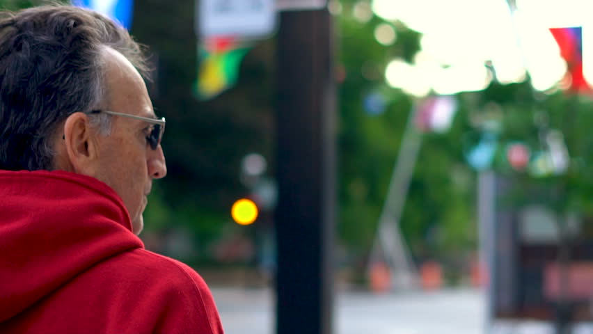Middle-Age man walking downtown Montreal along Sherbrooke street with international flags waving along (Cinematic slow motion footage)