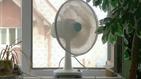 Domestic fan on window-sill in room in hot days / Household fan on windowsill in room