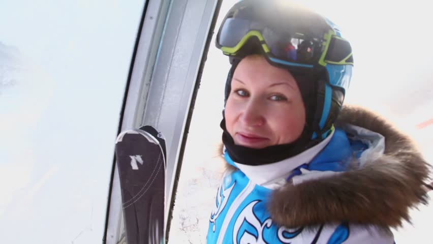Alone female skier in special clothing rides on funicular in mountains, small village shown from frozen window