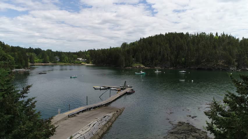 A moving aerial view of Seal Cove, an inland cove on Mt Desert Island Maine, with a small marina, homes on the cove and a picnic area, from the bay into the cove.
