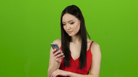 Asian girl looks on the phone, gossiping with her girlfriend. Green screen