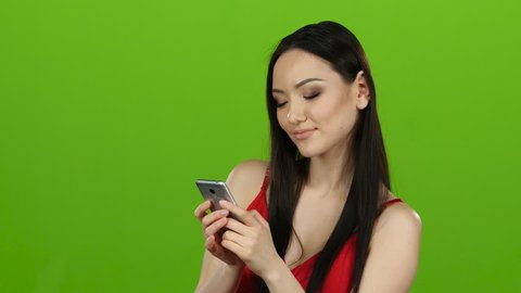 Girl of asian appearance flips through the phone photos and has fun. Green screen