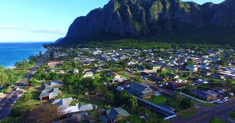 Highway Running Past Small Island Neighborhood in a Green Valley Surrounded by Imposing Green Mountains with Steep Cliff Walls - Aerial Footage on Oahu, Hawaii
