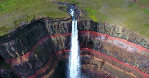 Green Plateau Waterfall Empties Over Red Banded Cliffs - Aerial Footage of Hengifoss Waterfall in Iceland